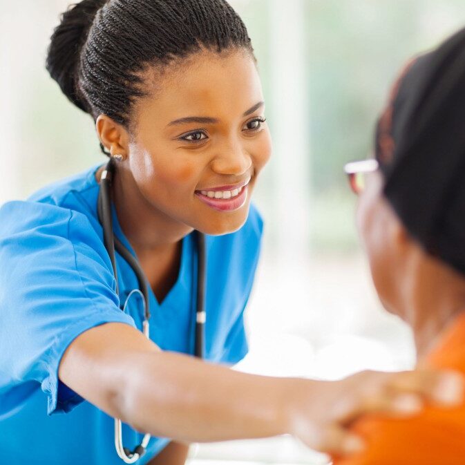 caring african medical nurse comforting senior patient in office